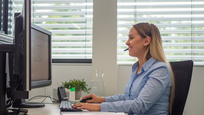 Blonde Frau sitzt am Schreibtisch mit Headset