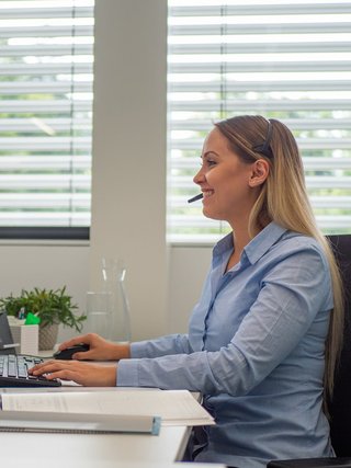 Blonde Frau sitzt am Schreibtisch mit Headset