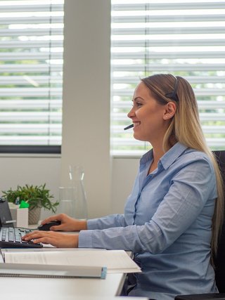 Blonde Frau sitzt am Schreibtisch mit Headset