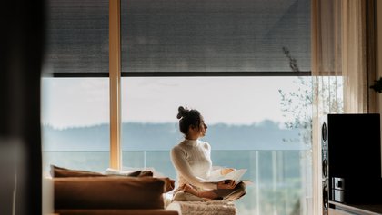 Frau liest sitzend auf Sofa. Im Hintgergrund sieht man Fensterfront mit Textilscreens.