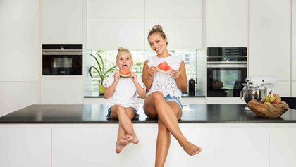 Frau und Mädchen sitzen in der Küche und essen Melone