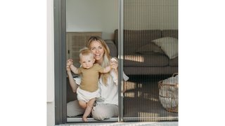 Blonde Frau mit Kind öffnet Insektenschutz Plissee Türe 