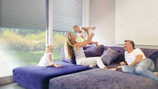 Rollladen Wohnzimmer Familie Familie sitzt auf lila Sofa vor halb offenen Rollladen