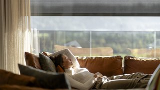Dame liegt auf der Couch, im Hintergrund sieht man den Sonnenschutz Sonnenschutz für das Wohnzimmer