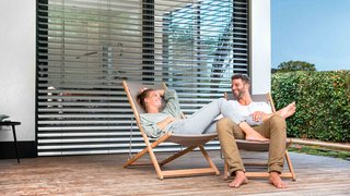 Sonnenschutz auf Terrasse Paar liegt auf Liegestuhl vor Fenster mit Raffstore