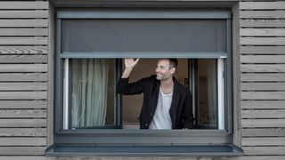 Blinos Rollo Holzfassade Mann blickt aus Fenster