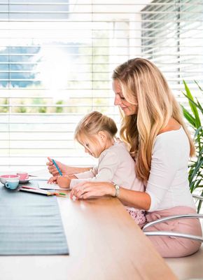 Frau sitzt mit Kind bei Tisch und malt