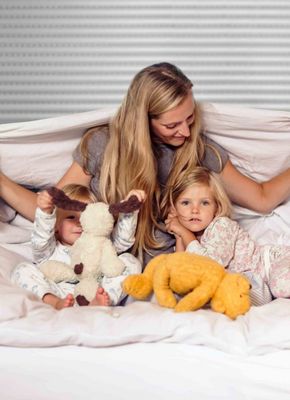 Frau mit Kindern unter der Bettdecke vor Rollladen