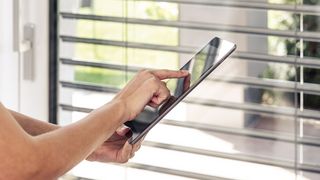 Smart Home Steuerung iPad Hand hält iPad und steuert damit Jalousie