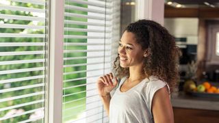 Sonnenschutz im Sommer Frau blickt durch geöffneten Raffstore nach draußen
