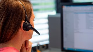 Dunkelhaarige Frau mit Headset vor PC