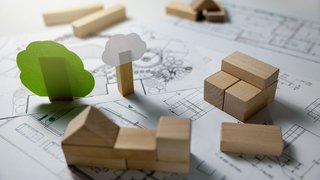 Ein nachhaltiges Haus wird auf einer gedruckten Planung durch stapelbare Holzsteinchen symbolisiert.