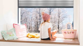 Mädchen vor Fenster mit Blick auf Winterlandschaft