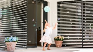 Kind spielt mit Luftballon vor Fenster mit Insektenschutz