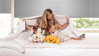 Familie sitzt auf Bett im Schlafzimmer vor Rollladen
