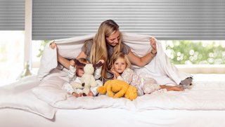 Redőnyök a hálószobában Család az ágyon a hálószobában a redőnyök előtt