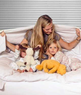 Familie sitzt auf Bett im Schlafzimmer vor Rollladen