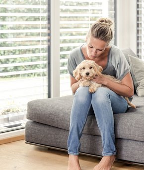 Frau und Hund sitzen im lichtdurchfluteten Wohnzimmer